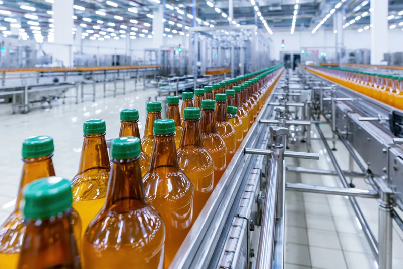 Amber glass bottles with green caps moving along conveyor line in factory