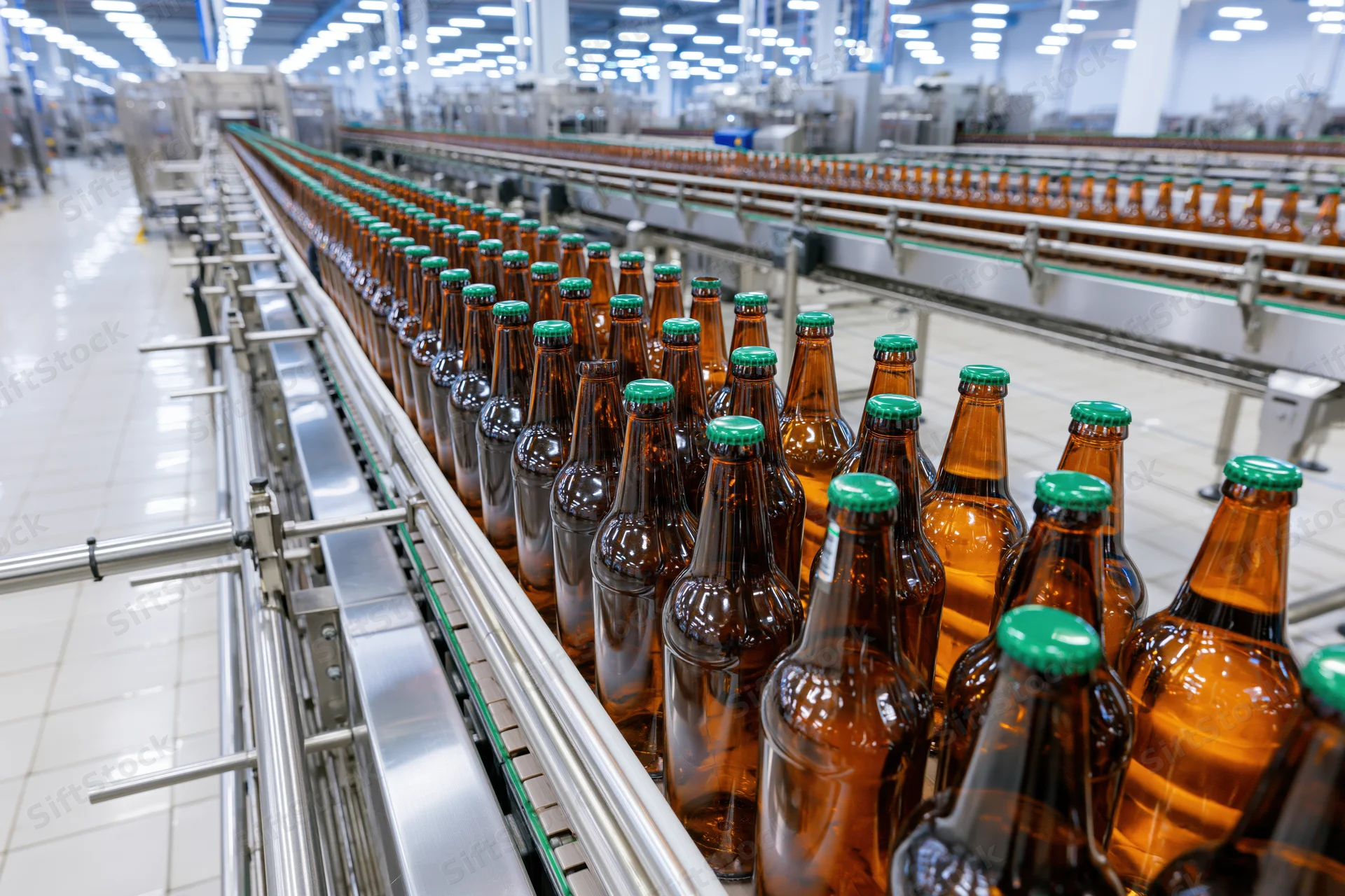 Amber glass beer bottles with green caps moving along conveyor line in factory