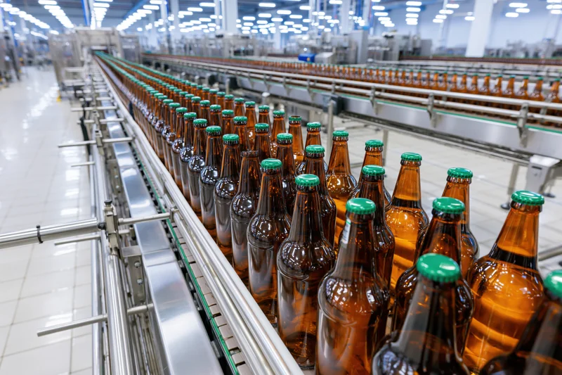 Amber glass beer bottles with green caps moving along conveyor line in factory