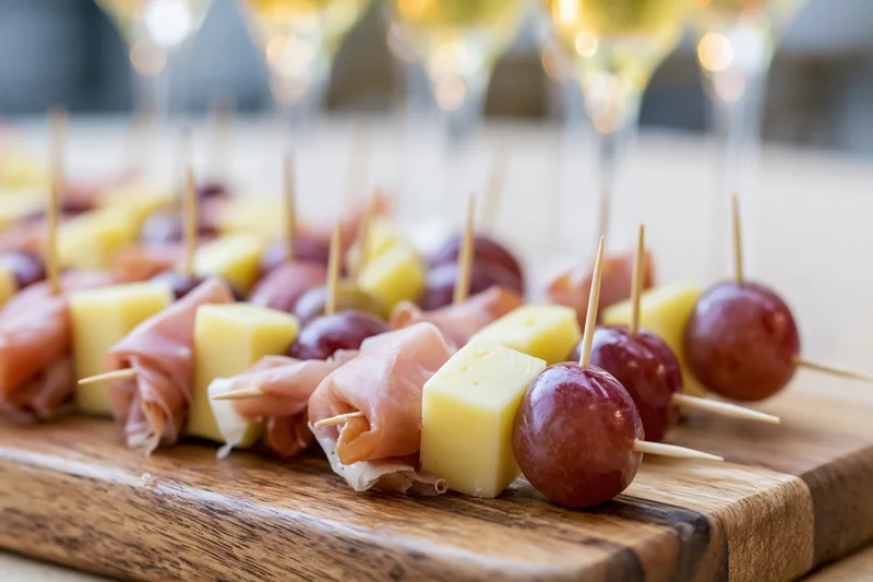 Appetizer skewers with cheese, grapes and prosciutto arranged on a wooden serving board