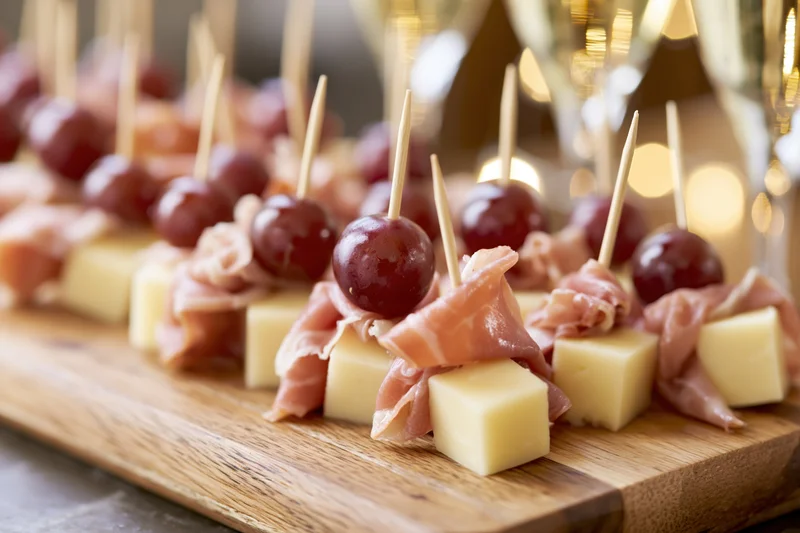 Rows of appetizer skewers with cheese, prosciutto and grapes on a wooden serving board