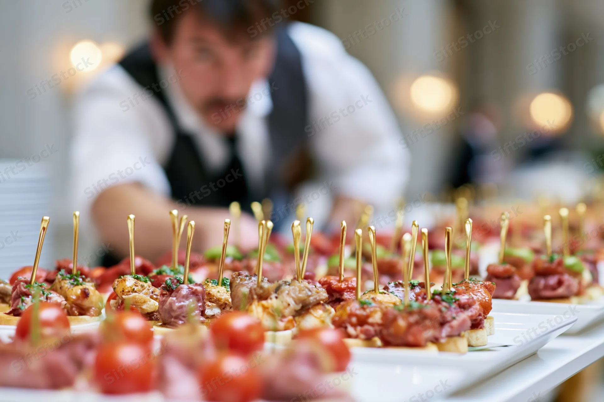 Rows of assorted canapes and finger food appetizers arranged on white plates with a server in the background