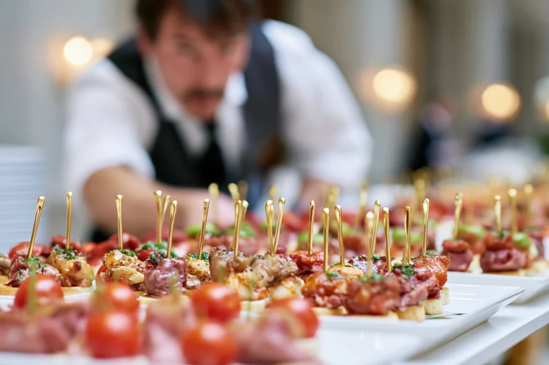 Rows of assorted canapes and finger food appetizers arranged on white plates with a server in the background
