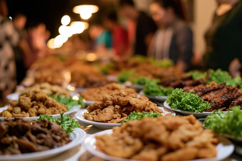 Rows of fried and grilled street food with fresh lettuce on plates at a social gathering indoors at night