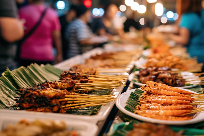 Grilled prawns and meat skewers arranged on banana leaves and white plates at a night market stall