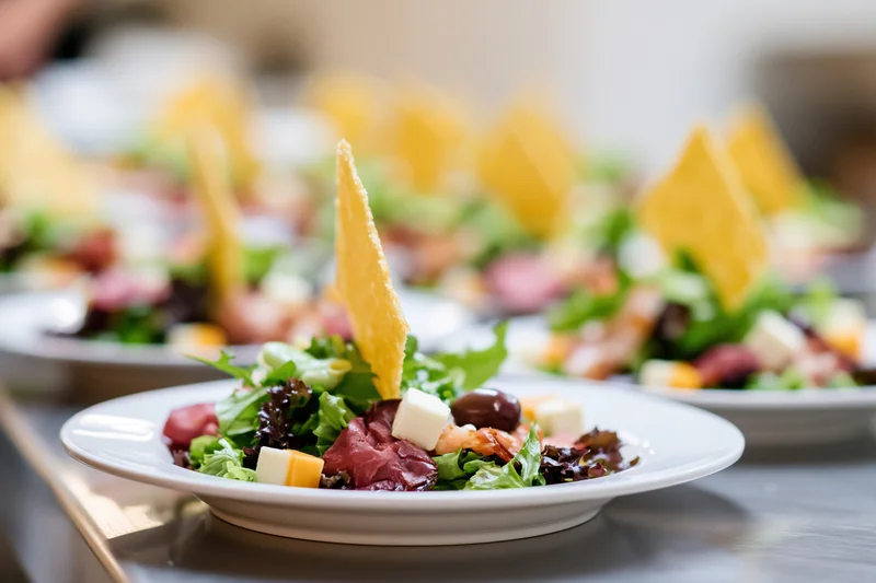Rows of identical appetizer salads with cheese and meat on white plates arranged on a stainless steel tray