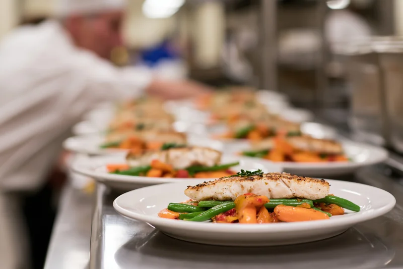 Rows of identical plated fish dishes lined up on a stainless steel counter in a restaurant kitchen