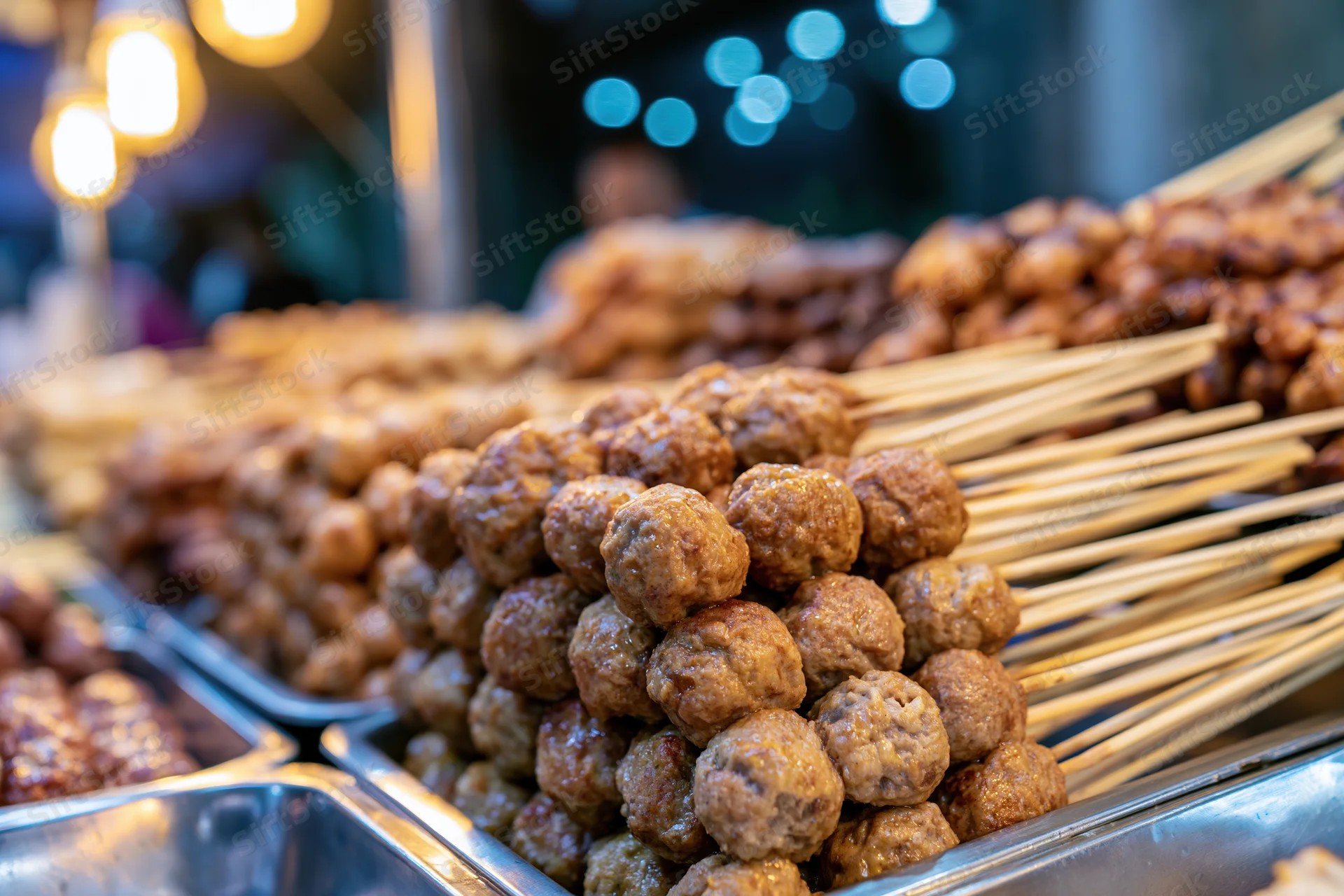 Rows of skewered meatballs displayed in stainless steel trays at a night market stall