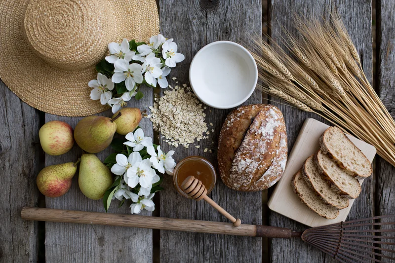 Rustic harvest flat lay with bread, pears, honey, wheat, and flowers on weathered wooden table