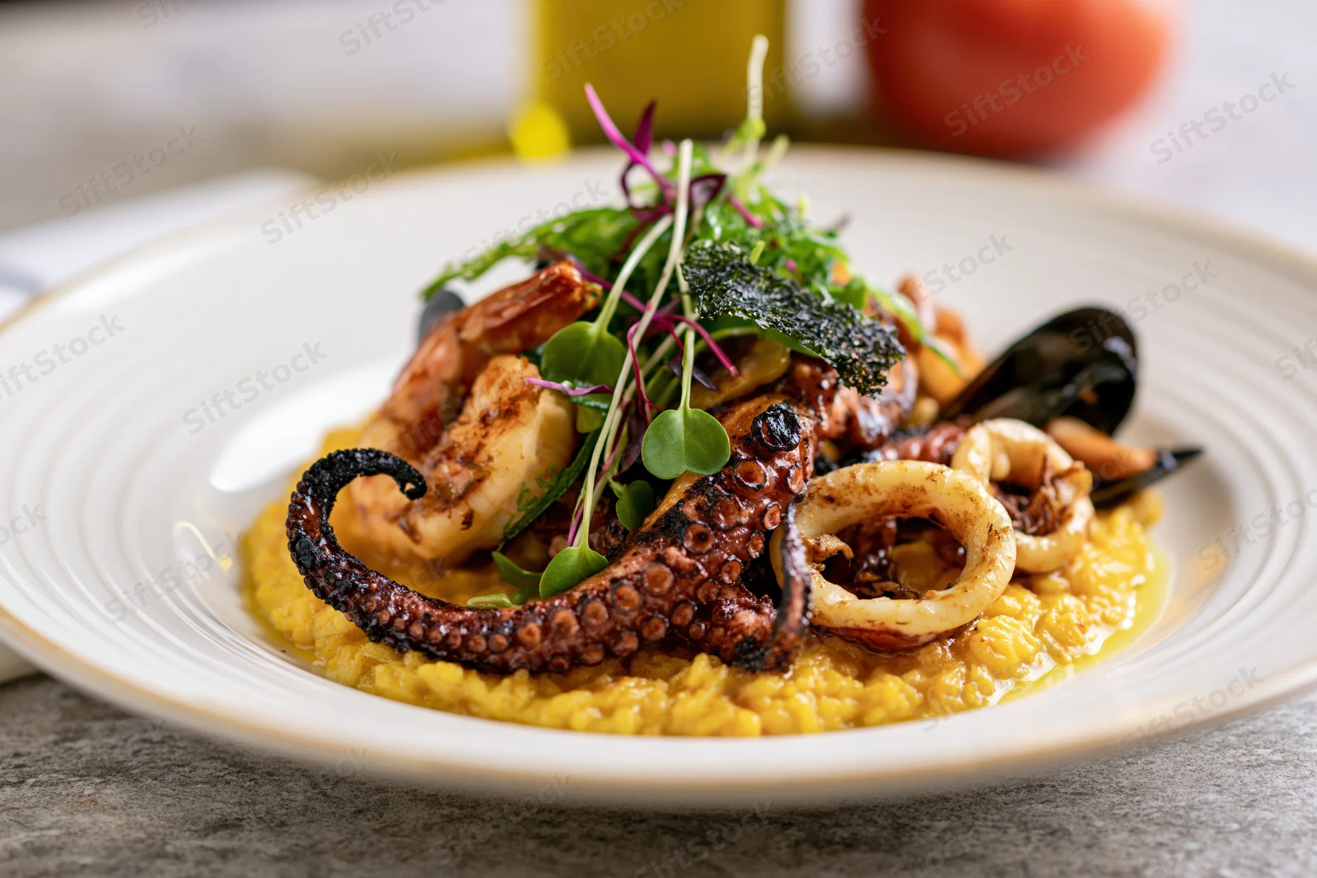 Grilled octopus and shellfish served on a yellow risotto base with microgreens garnish on a white ceramic plate