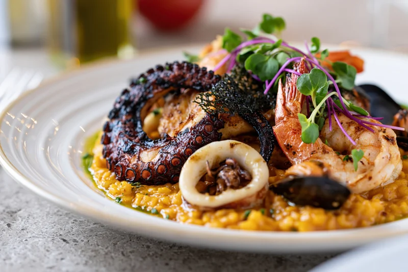 Grilled octopus and shrimp served on a saffron risotto with microgreens on a white ceramic plate