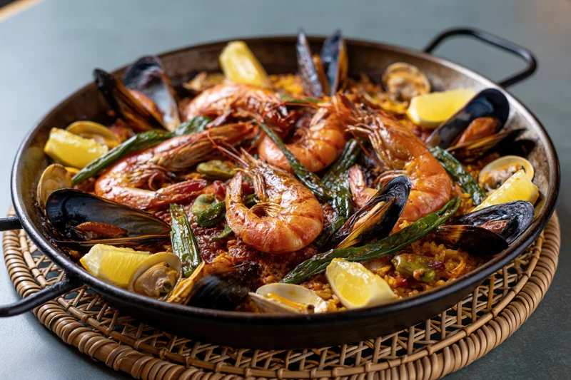 Seafood paella with shrimp, mussels, clams and lemon in a wide dark steel pan on a wicker placemat