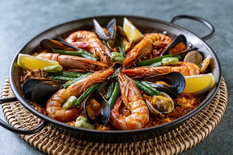 Seafood paella with shrimp and mussels in a dark steel pan on a woven placemat