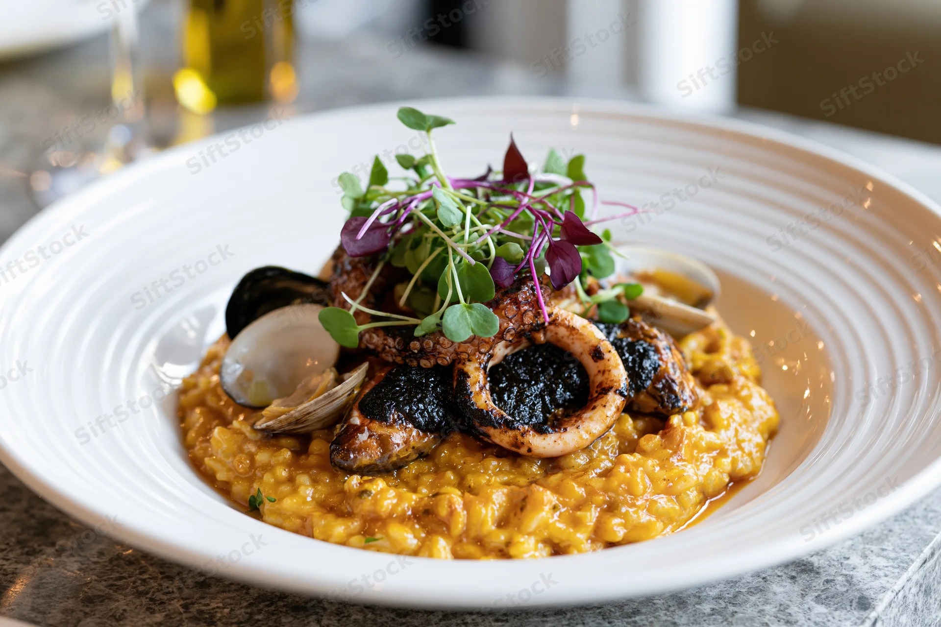 Seafood risotto with grilled octopus and clams topped with microgreens served in a wide white ceramic bowl on a marble table