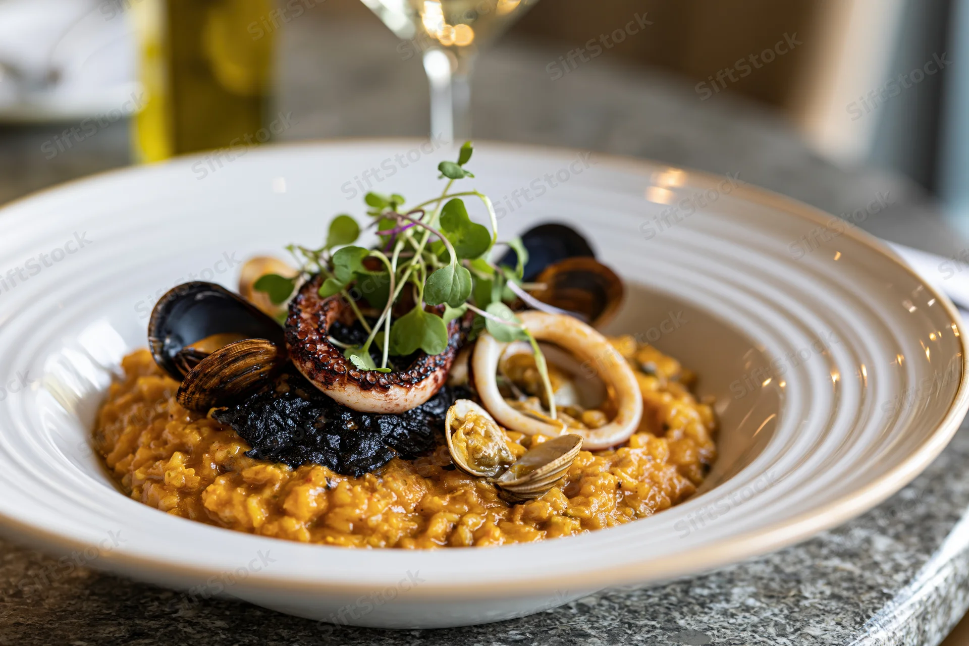 Seafood risotto with octopus, squid, mussels and microgreens in a white ceramic bowl on a marble table