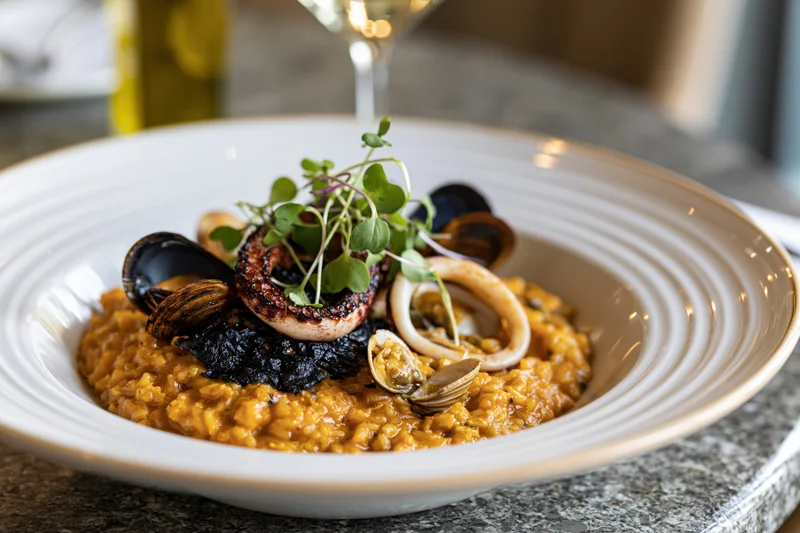 Seafood risotto with octopus, squid, mussels and microgreens in a white ceramic bowl on a marble table
