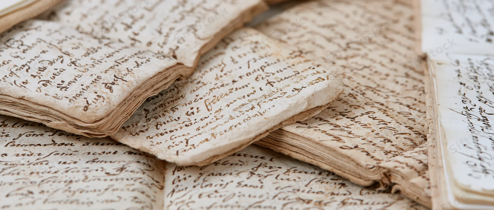 Aged handwritten letters and an open journal spread in a stack, showing cursive script on yellowed paper