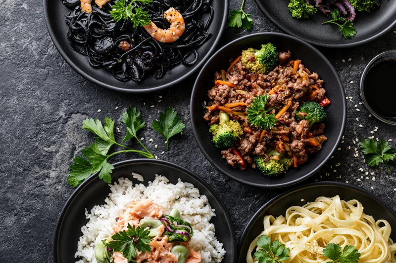 Several dark ceramic plates with different meals arranged on a black textured surface