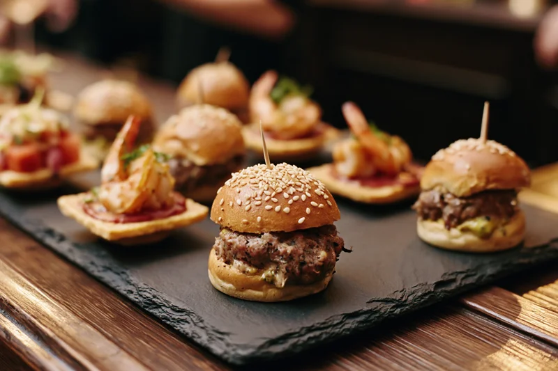 Gourmet mini sliders and bite-sized appetizers arranged on a slate tray on a wooden table