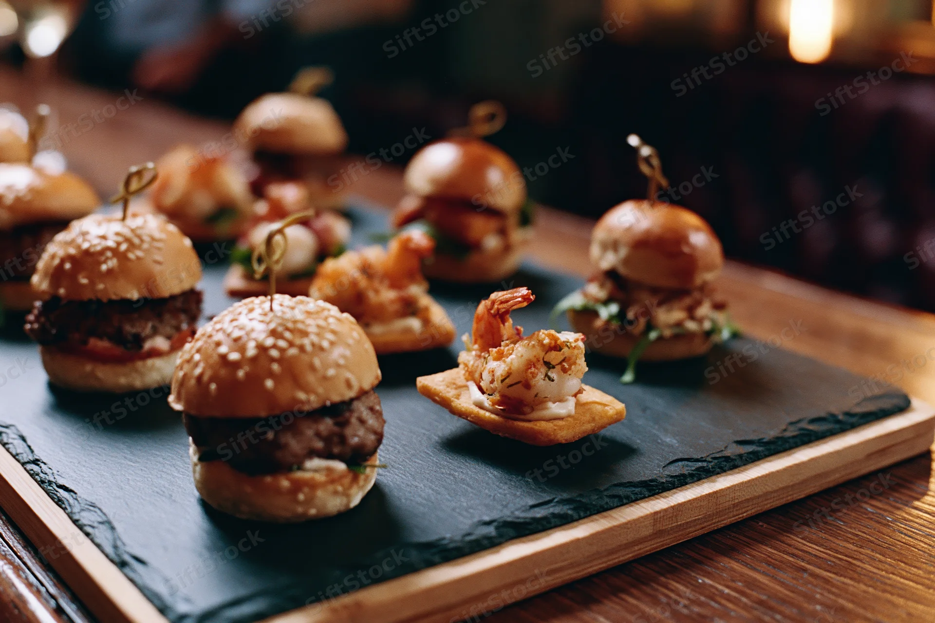 Gourmet mini sliders and bite-sized appetizers arranged on a slate platter on a wooden table