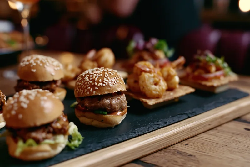 Gourmet mini sliders and bite-sized appetizers arranged on a slate tray on a wooden table