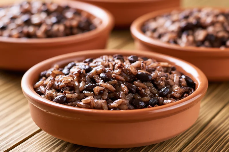 Terracotta bowls filled with gallo pinto rice and black beans on a wooden surface