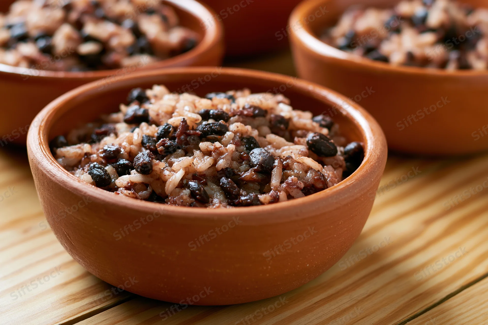 Terracotta bowls filled with rice and black beans on a wooden surface