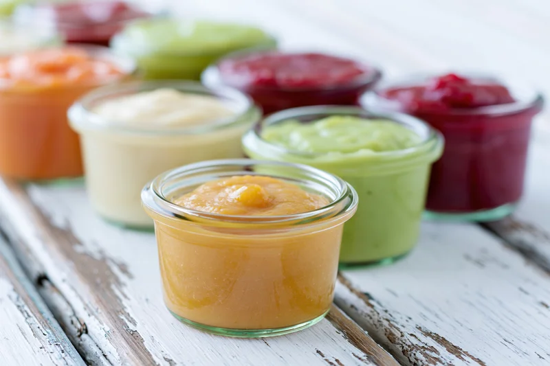 Small glass jars filled with colorful baby food puree arranged on a rustic white wooden table