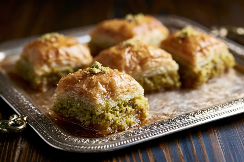 Square pistachio baklava pieces arranged on an ornate silver tray on a dark wooden table