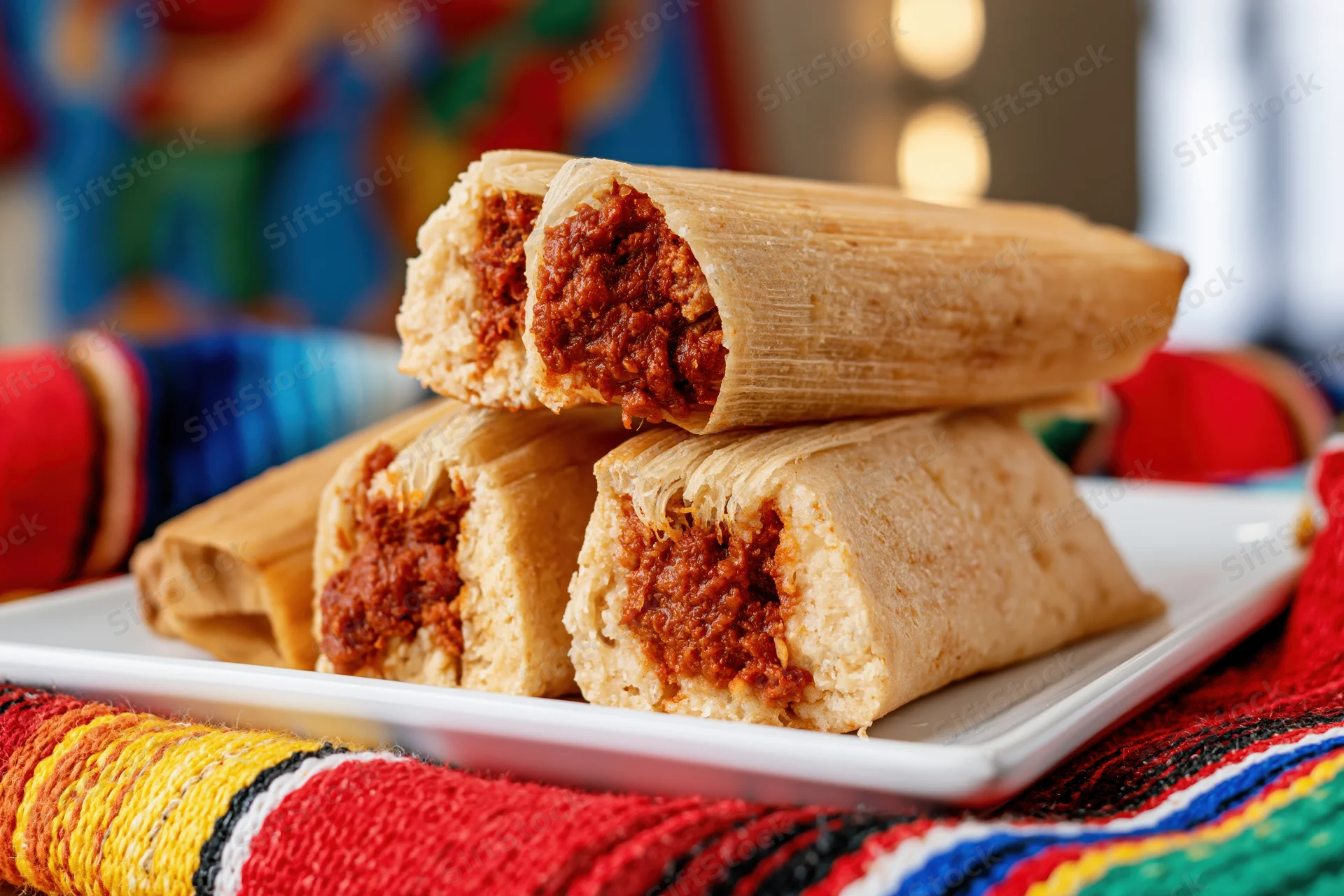 Stacked cross-cut tamales on a white plate resting on a colorful woven textile