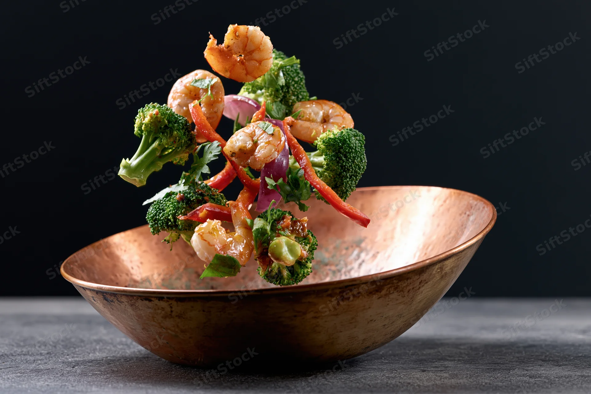 Shrimp and vegetables falling into a copper bowl midair