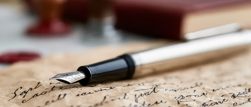 Silver and black fountain pen resting on aged parchment paper with handwritten script