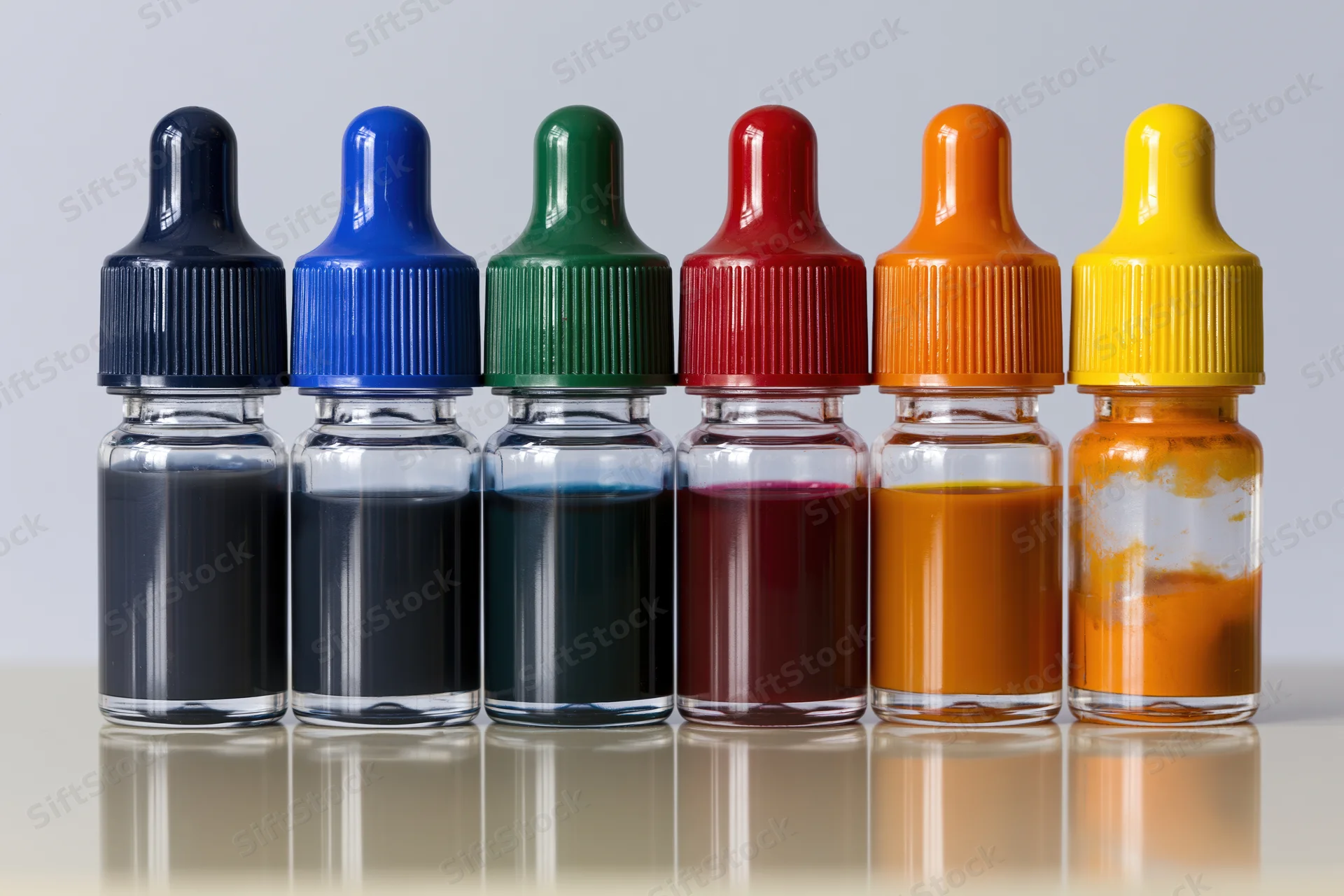 Six glass dropper bottles filled with colored paint arranged in a row on a reflective white surface