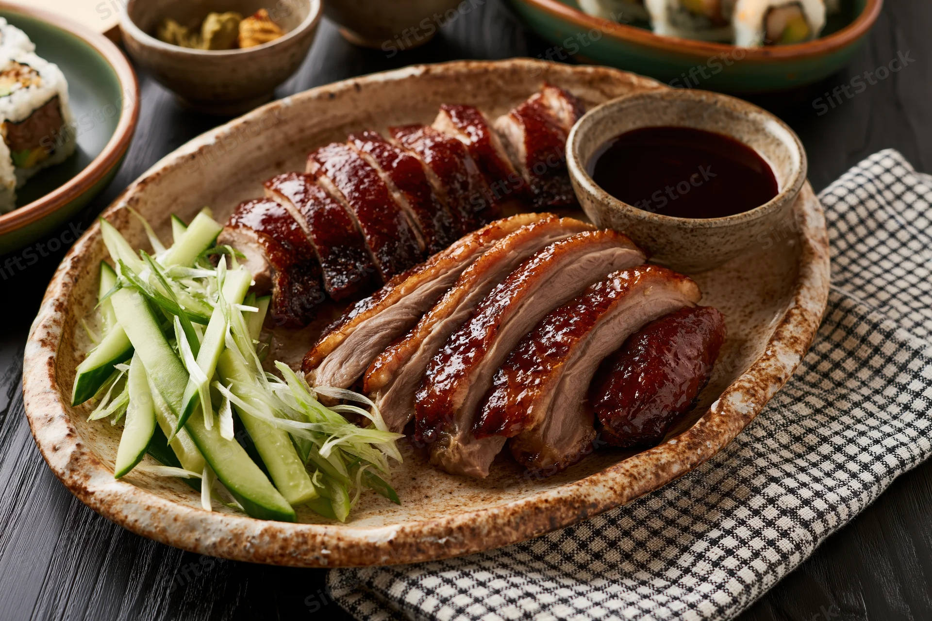 Sliced peking duck arranged on a rustic ceramic plate with cucumber and scallion garnish and dipping sauce on a dark wooden table