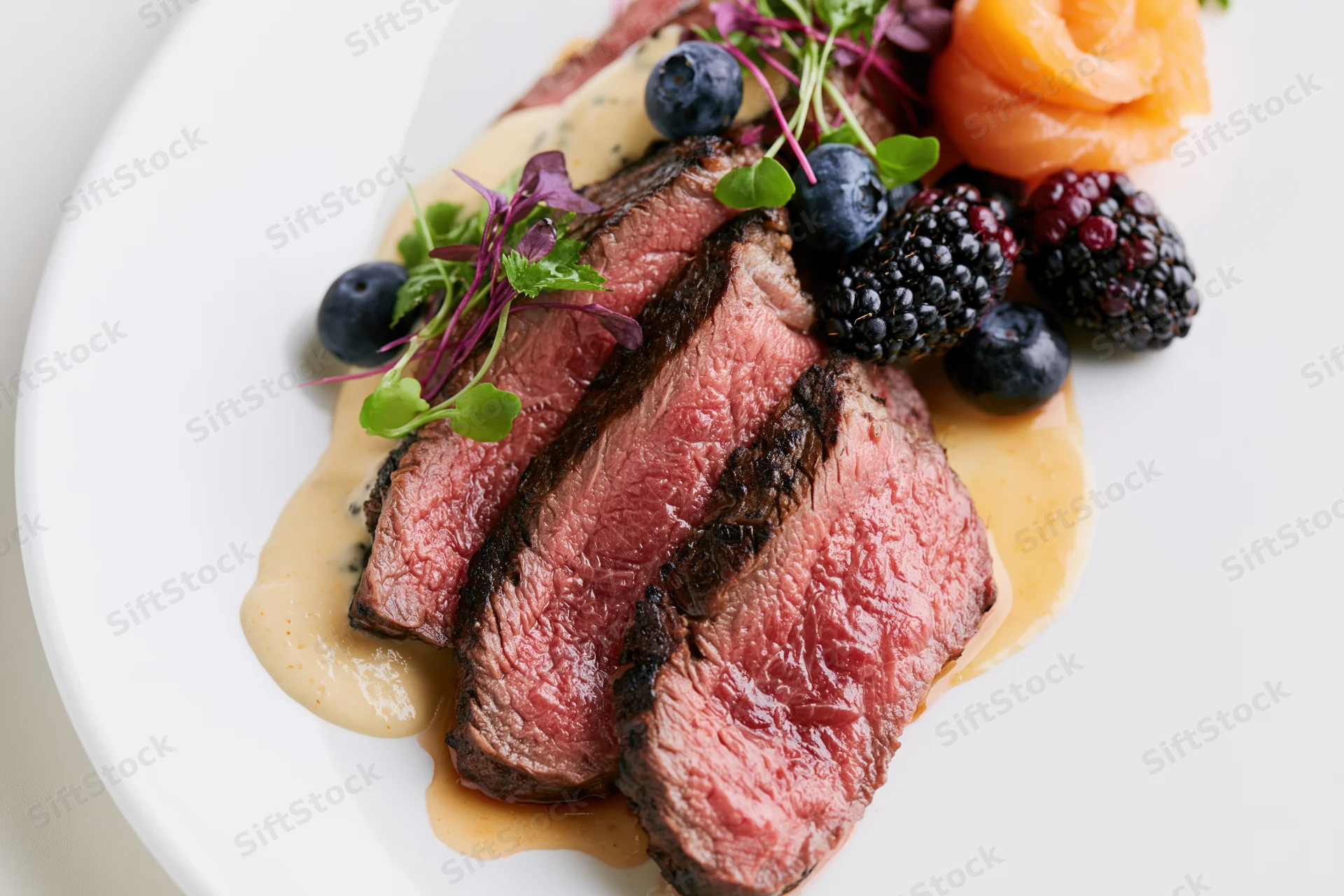 Sliced medium-rare beef tenderloin with berries and microgreens on a white plate