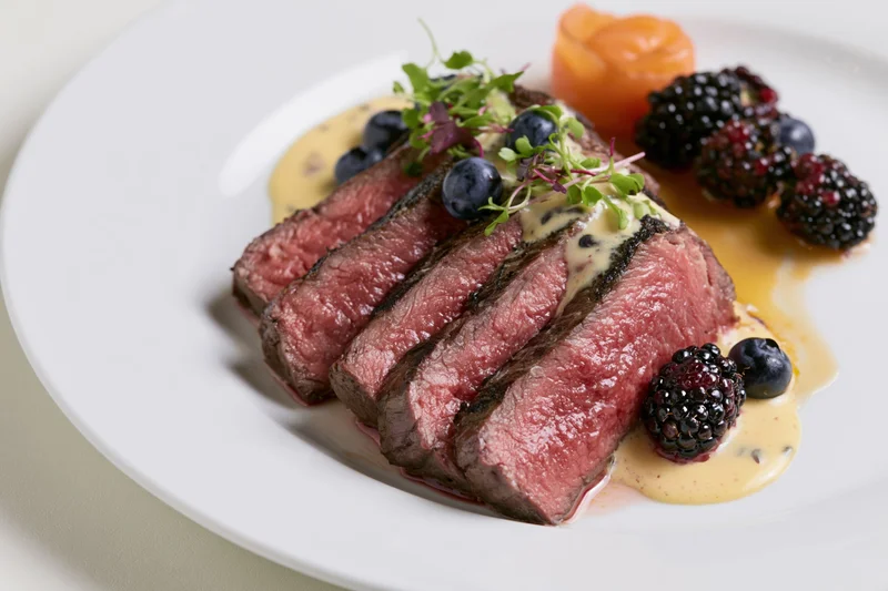 Sliced medium-rare beef tenderloin fanned on a white plate with fruit and sauce garnish