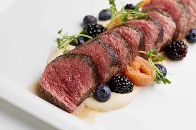 Sliced medium-rare beef tenderloin arranged on a white plate with berries and sauce