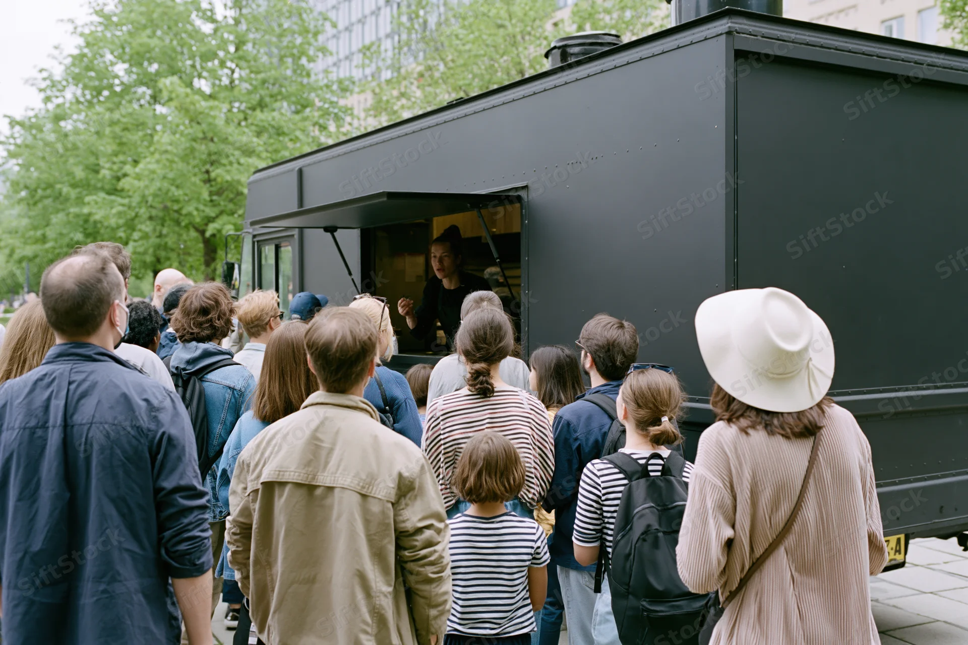 Crowd of adults and children waiting in line at a black food truck on a city sidewalk