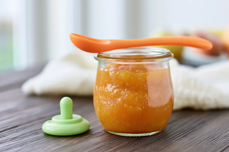 Jar of Orange Baby Food On Wooden Table With Green Lid Nearb