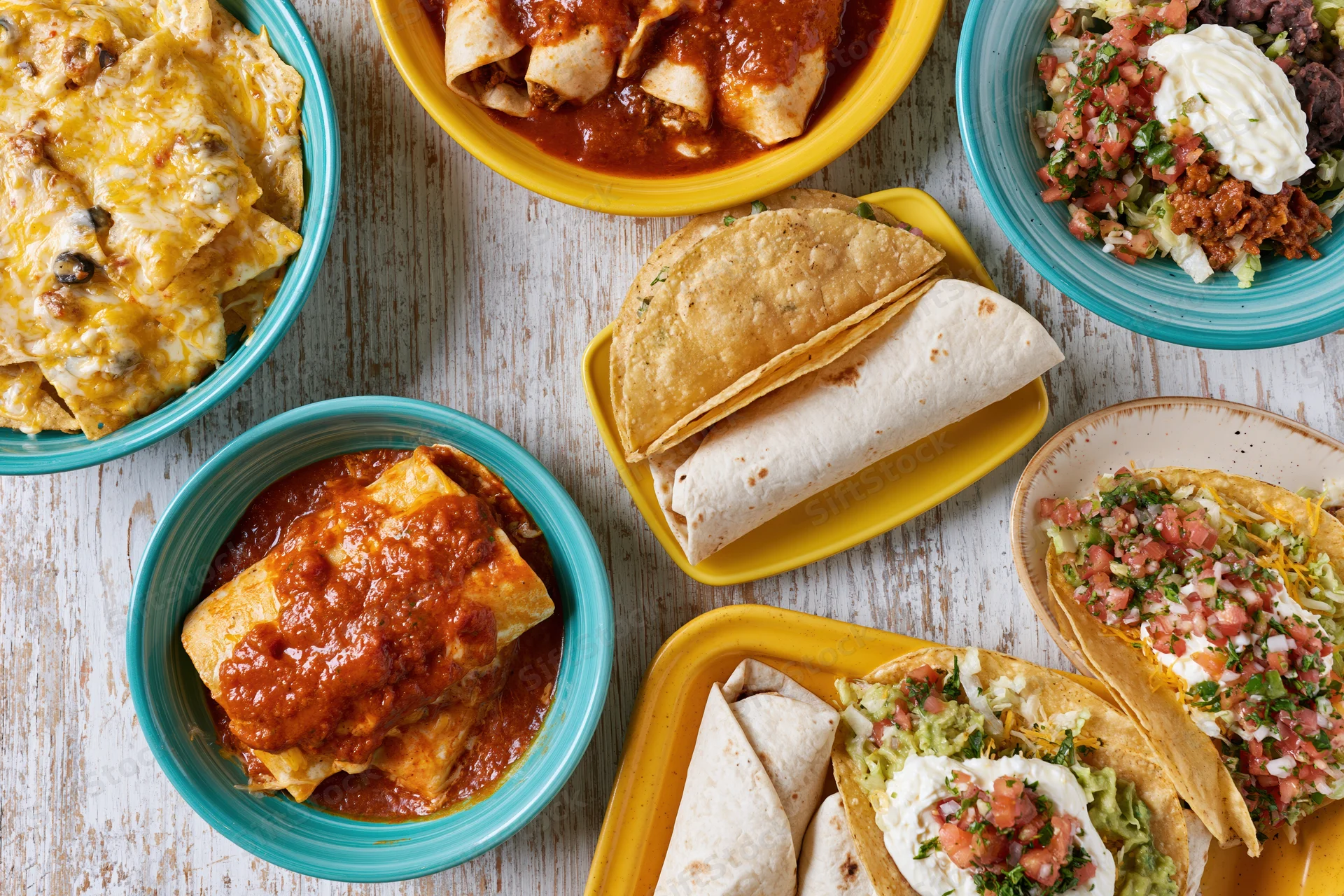 Spread of mexican dishes including tacos, burritos, enchiladas and nachos on a whitewashed wood table