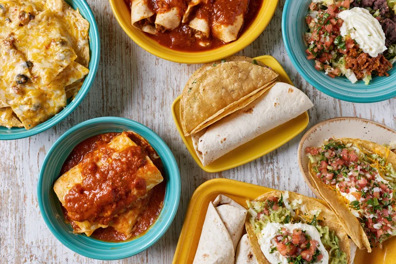 Spread of mexican dishes including tacos, burritos, enchiladas and nachos on a whitewashed wood table