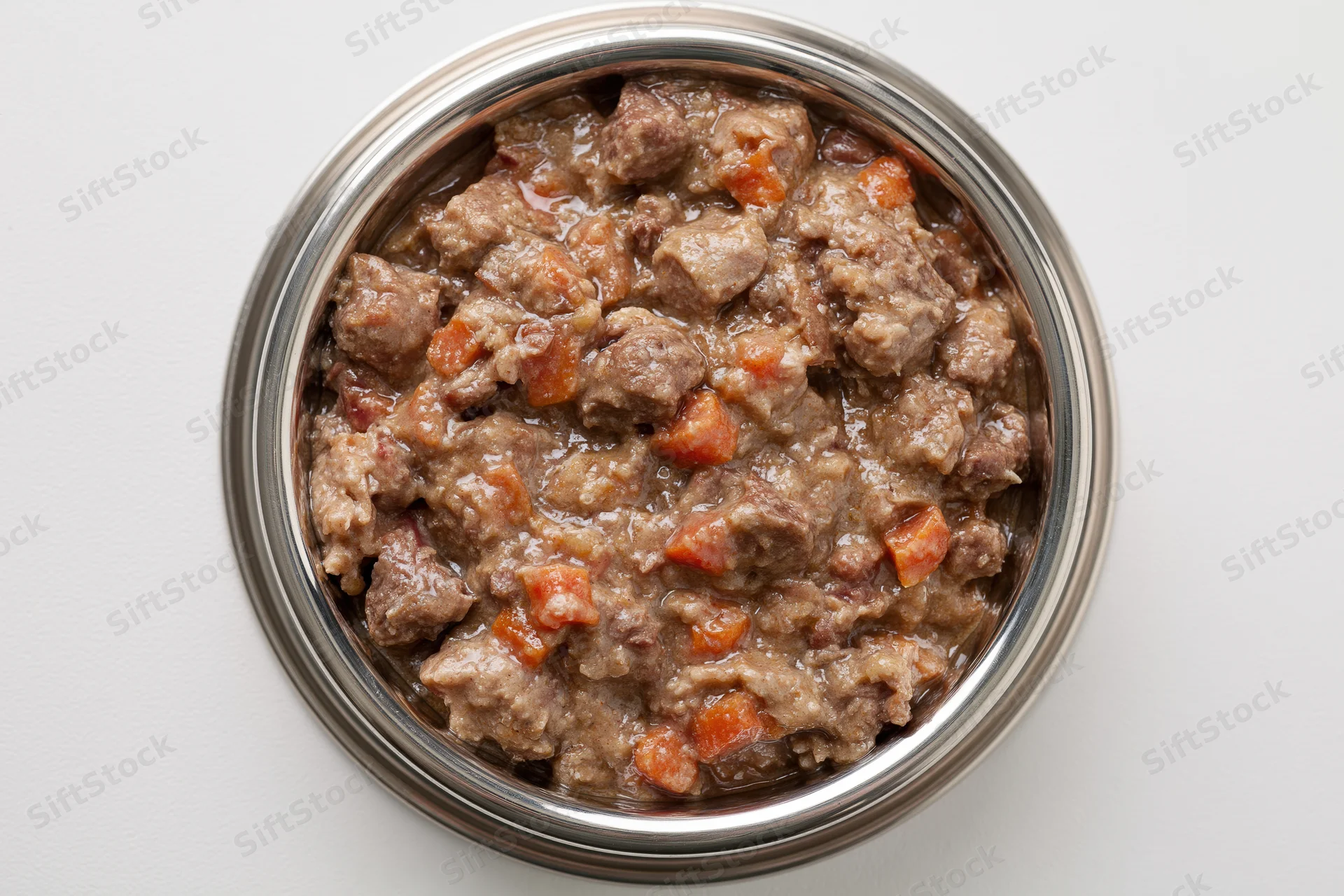 Chunky wet dog food in a stainless steel bowl on white surface