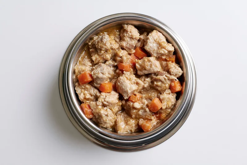 Chunky wet dog food in a stainless steel bowl on white surface