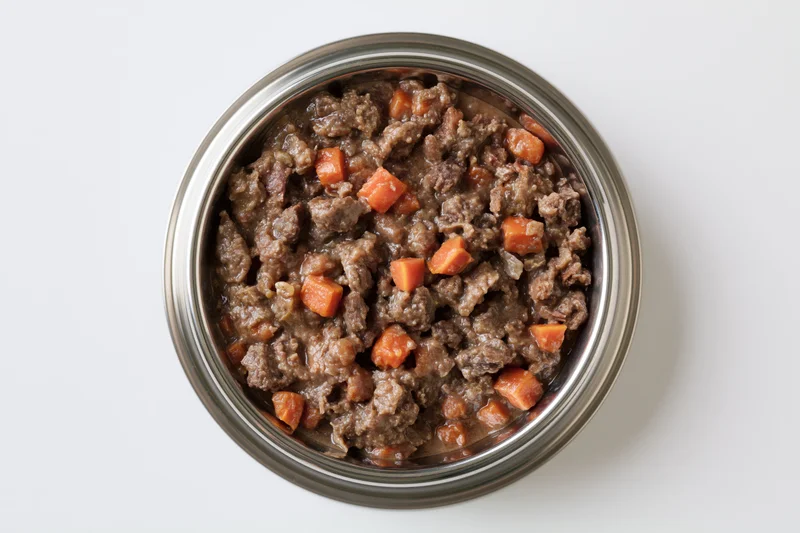 Chunky wet dog food in a stainless steel bowl viewed from above