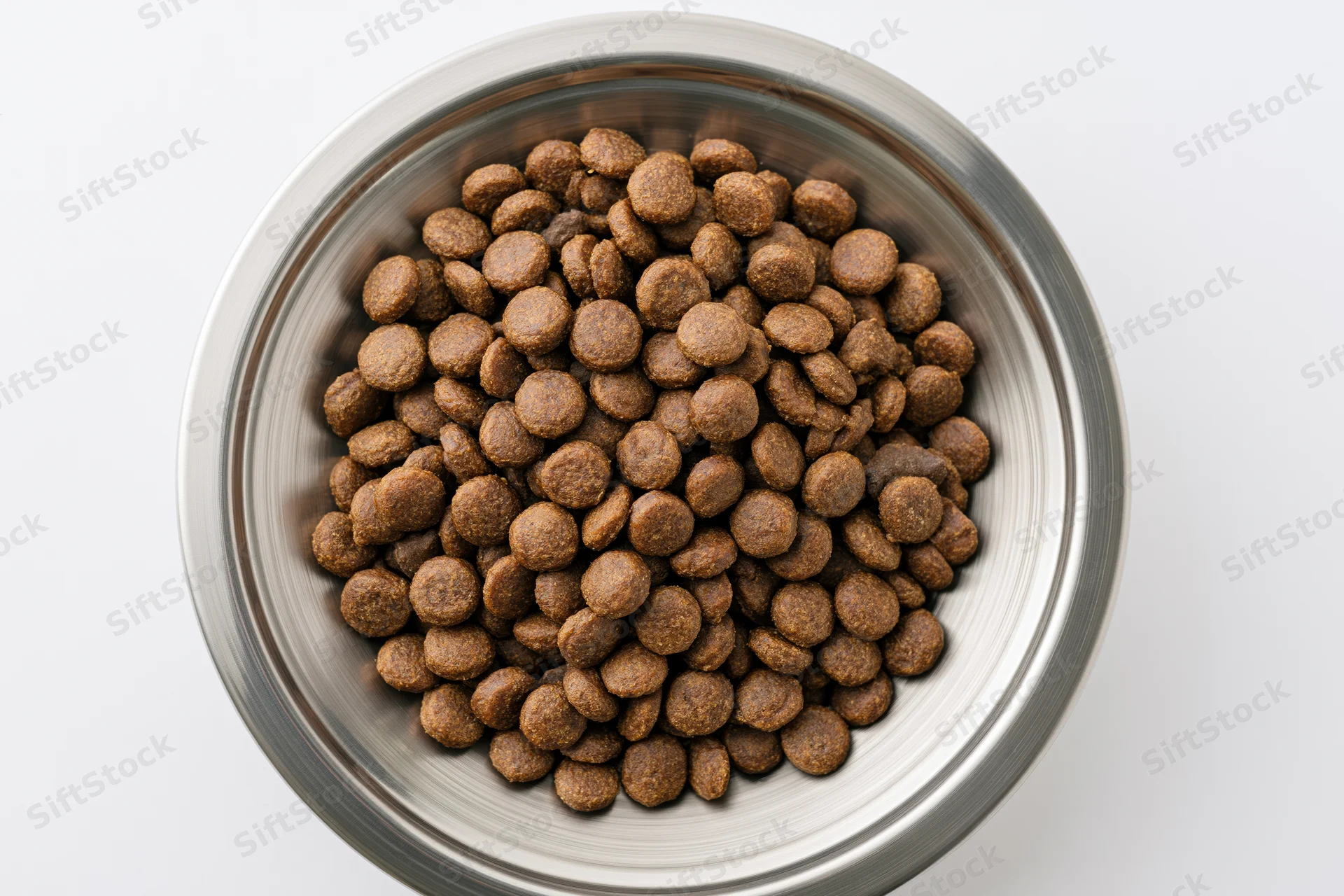 Dry kibble in a stainless steel bowl viewed from above on white background