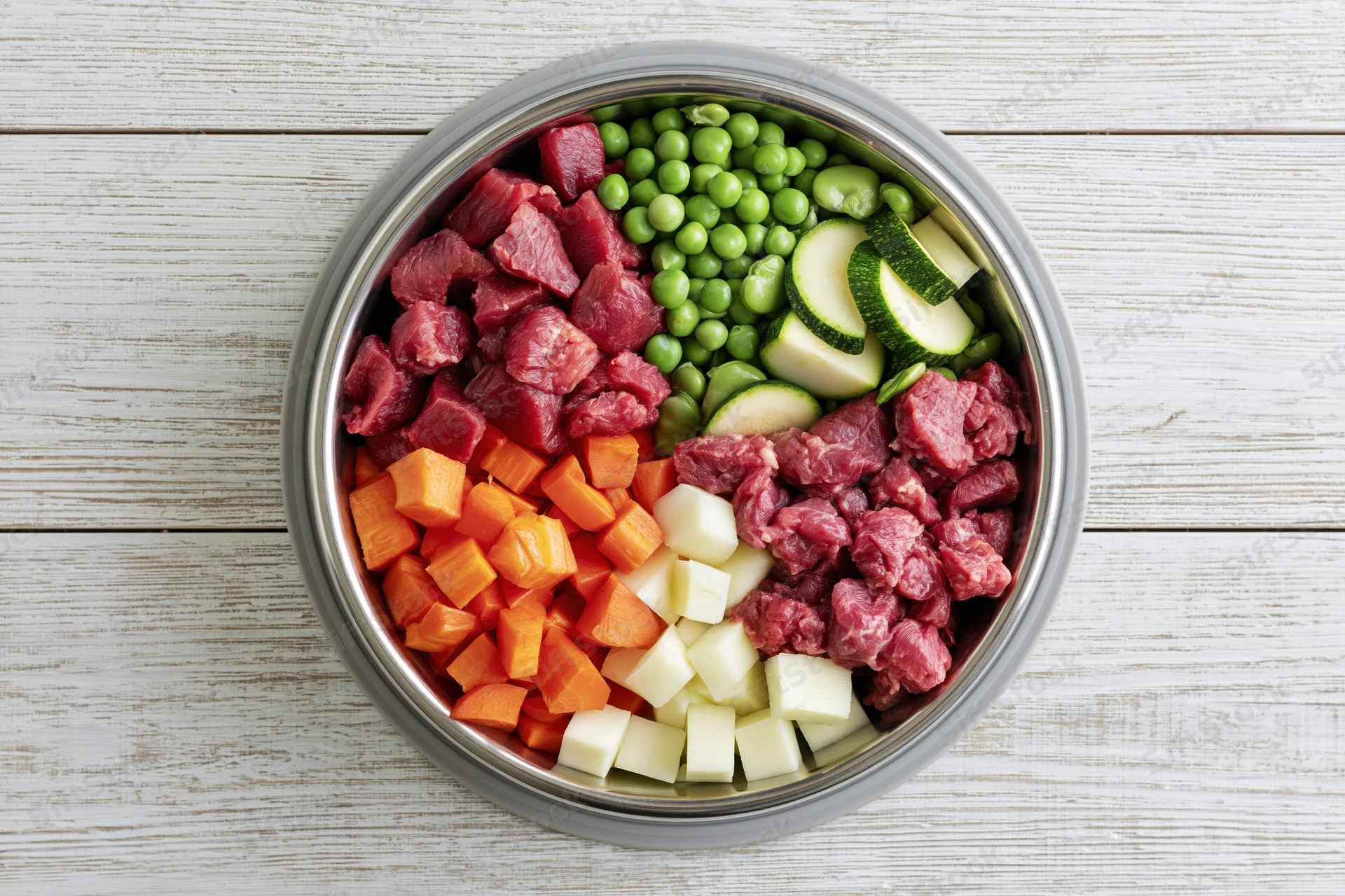 Raw dog food ingredients arranged in a stainless steel bowl on a white wooden surface