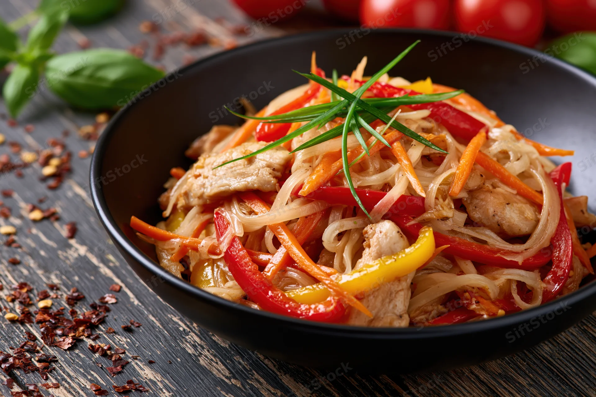 Stir-fried rice noodles with chicken and vegetables in a black bowl on a dark wooden table