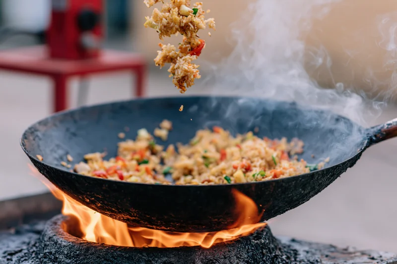 Stir-fried rice and vegetables being tossed in a wok over an open flame