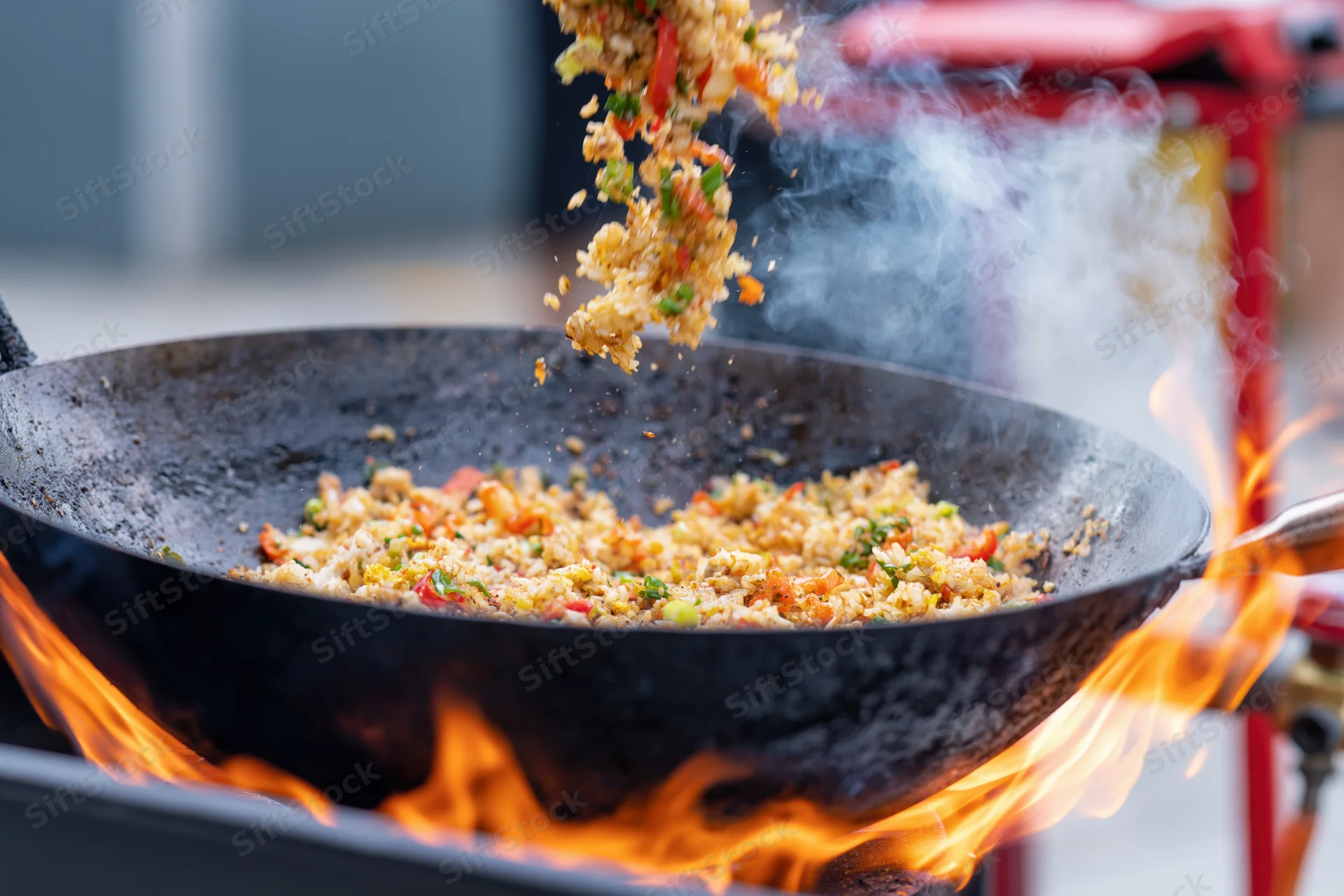 Stir-fried rice and vegetables being tossed in a wok over open flames