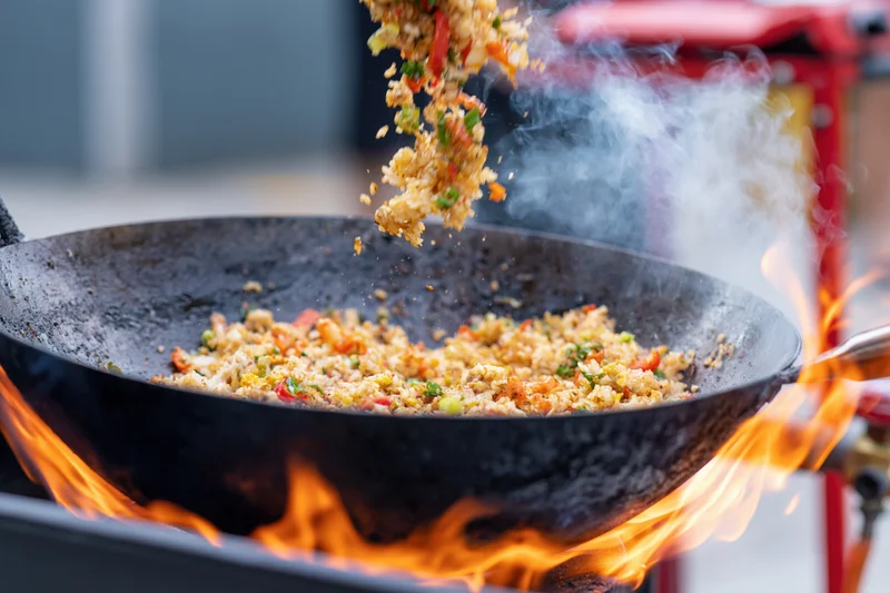 Stir-fried rice and vegetables being tossed in a wok over open flames
